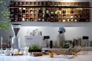 A modern kitchen with a coffee machine, a shelf of kitchenware, and a variety of plants.