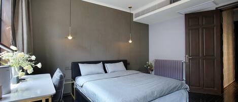 A modern bedroom with a large bed, a desk with a chair, and a decorative vase of flowers.