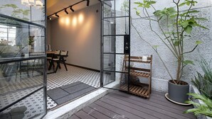 An open glass door leading to a dining area with a table and chairs, a wooden bench, and a potted plant. - Hills boutique (Shanghai)