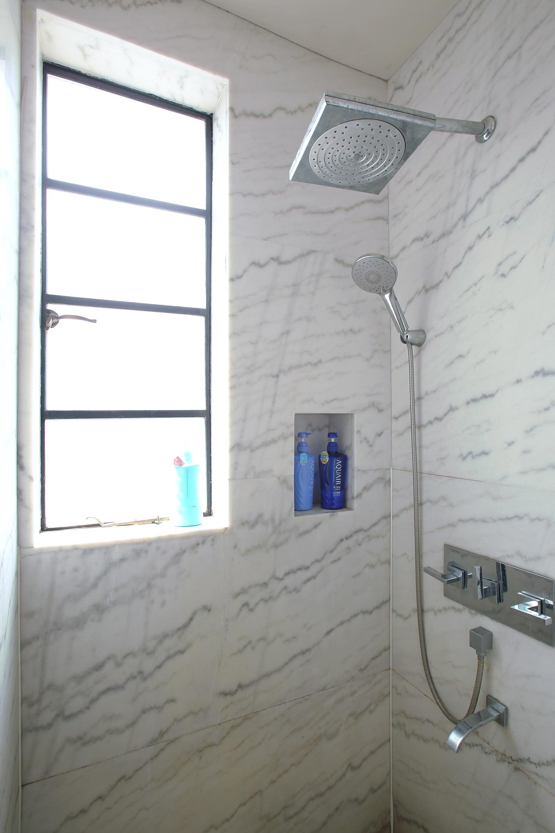 Un baño con ducha, ventana y estante con artículos de aseo.