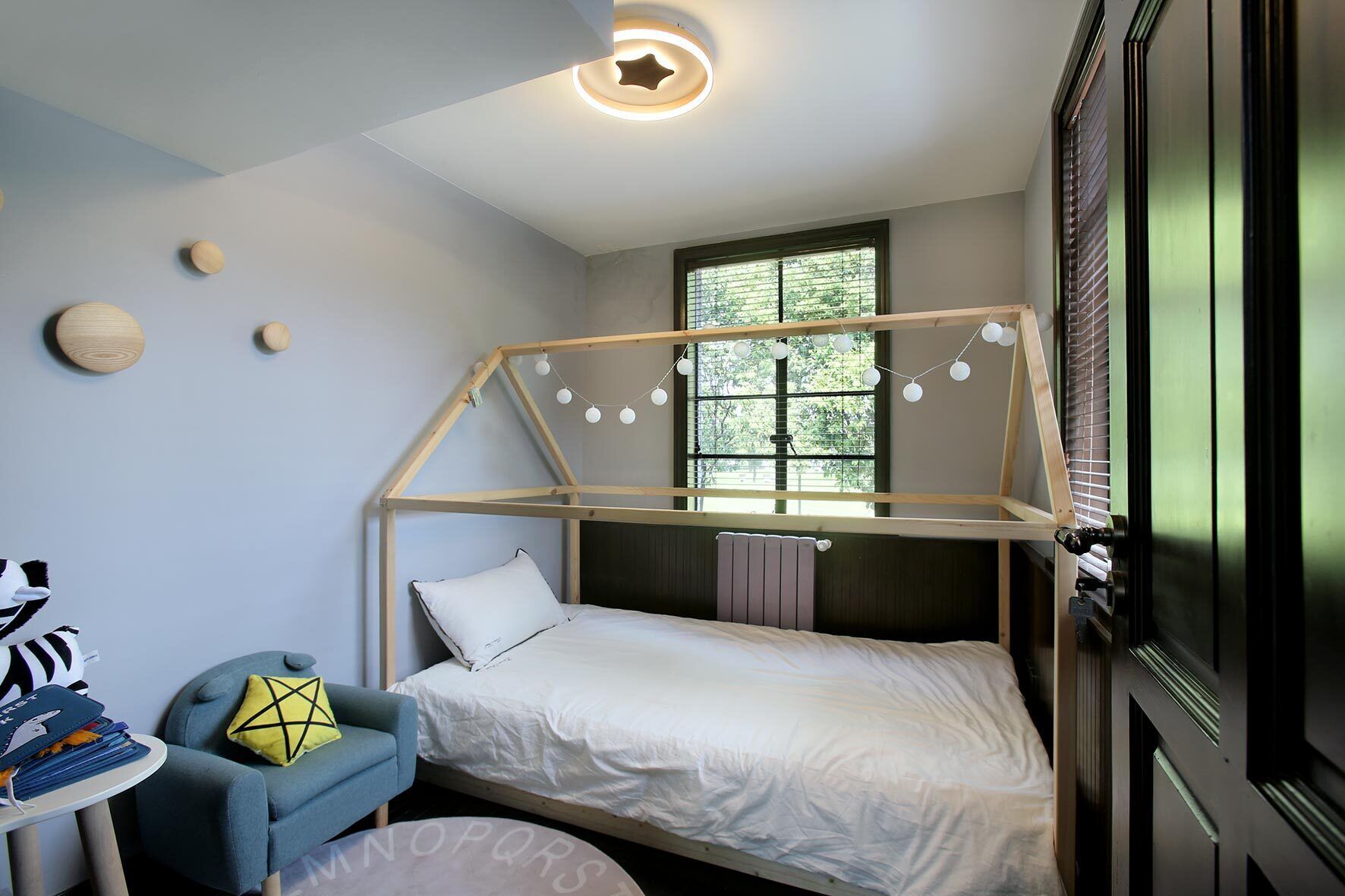 A bedroom with a wooden bed frame, a desk with a chair, and a window with blinds.