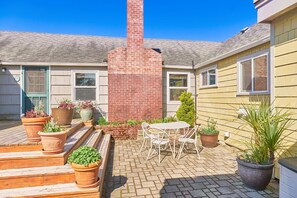 A patio area with a brick chimney, potted plants, and a white outdoor table and chairs. - PICKLEBALL! Walk to Beach, Fireplace, BBQ (ANC#9) (Long Beach)
