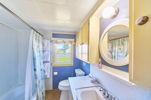 A compact bathroom with a shower, toilet, sink, and a window with a view of a house. - PICKLEBALL! Walk to Beach, Fireplace, BBQ (ANC#10) (Long Beach)