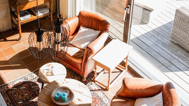 Un salon moderne doté d’une grande porte vitrée donnant sur une terrasse, aménagée avec des fauteuils en cuir et une petite table.