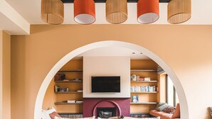 Een gezellige woonkamer met een open haard, boekenplanken en een aan de muur bevestigde televisie.