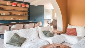 Een moderne woonkamer met een witte zithoek, een houten salontafel en een keuken op de achtergrond.