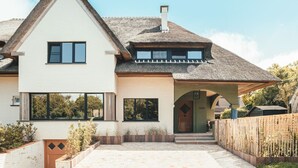 Een modern huis met twee verdiepingen, een ruime veranda, een rieten dak en een houten hek.