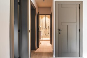 A hallway leading to a shower area with a glass door, a wooden floor, and a closed door on the right.