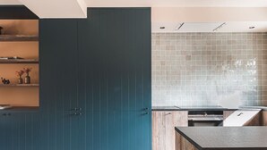 Een moderne keuken met blauwgroene kastjes, een betegelde achterwand en een houten aanrecht.