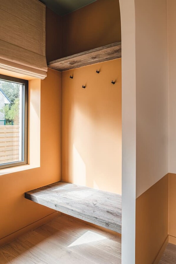 A corner room with a wooden bench, a window, and a wall-mounted light fixture.
