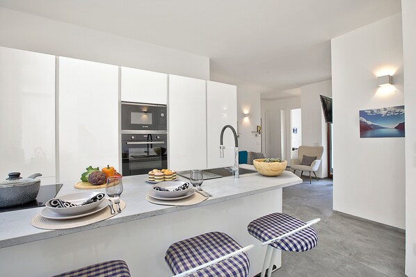 A modern kitchen with white cabinetry, a central island with bar stools, a microwave, and a sink. - Quiet Oasis In Riva Heart (Riva del Garda)