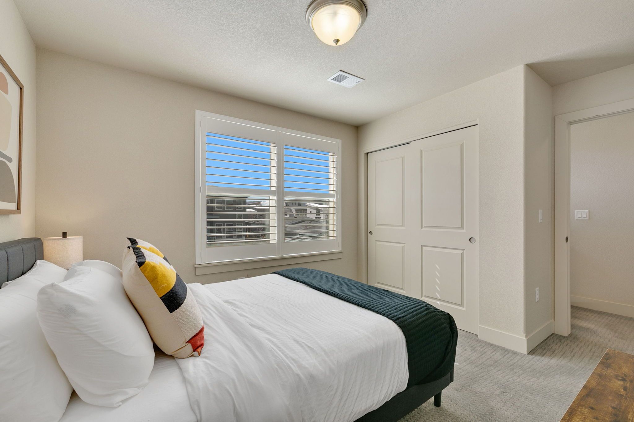 A bedroom with a bed, a window with blinds, a door, and a ceiling light fixture.