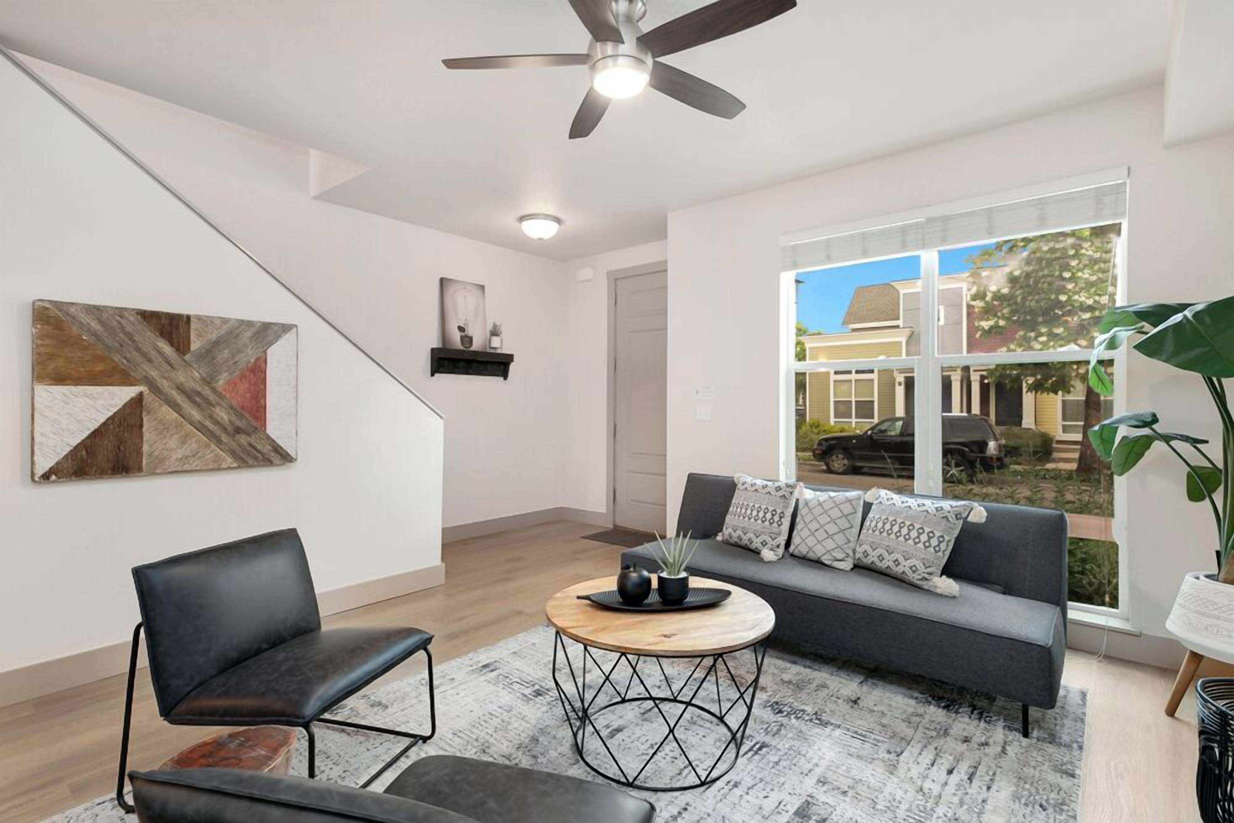 A modern living room with a sofa, two chairs, a coffee table, and a ceiling fan.