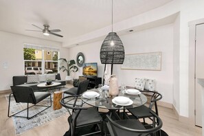 Un espace repas moderne avec une table ronde en verre, des chaises noires et un luminaire suspendu noir.