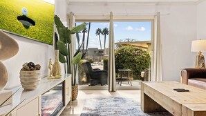 A modern living room with a wooden coffee table, a sofa, and a large window offering a view of a garden and palm trees.