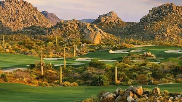 A golf course with rocky mountains in the background, well-maintained grass, and sand bunkers.
