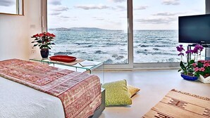 A bedroom with a large window overlooking the sea, a bed, a small table with a red tray, and a television. - VILLA DIAMANTE - Seven Bedroom Villa, Sleeps 14 (Stintino)
