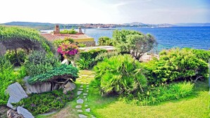 A lush garden with a stone pathway leading to a building with a red-tiled roof, overlooking a body of water and distant hills. - VILLA DIAMANTE - Seven Bedroom Villa, Sleeps 14 (Stintino)