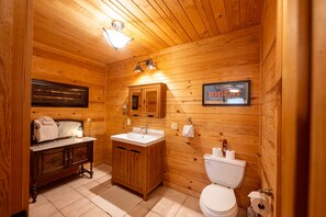 Un baño con paneles de madera, un lavabo, tocador e inodoro.