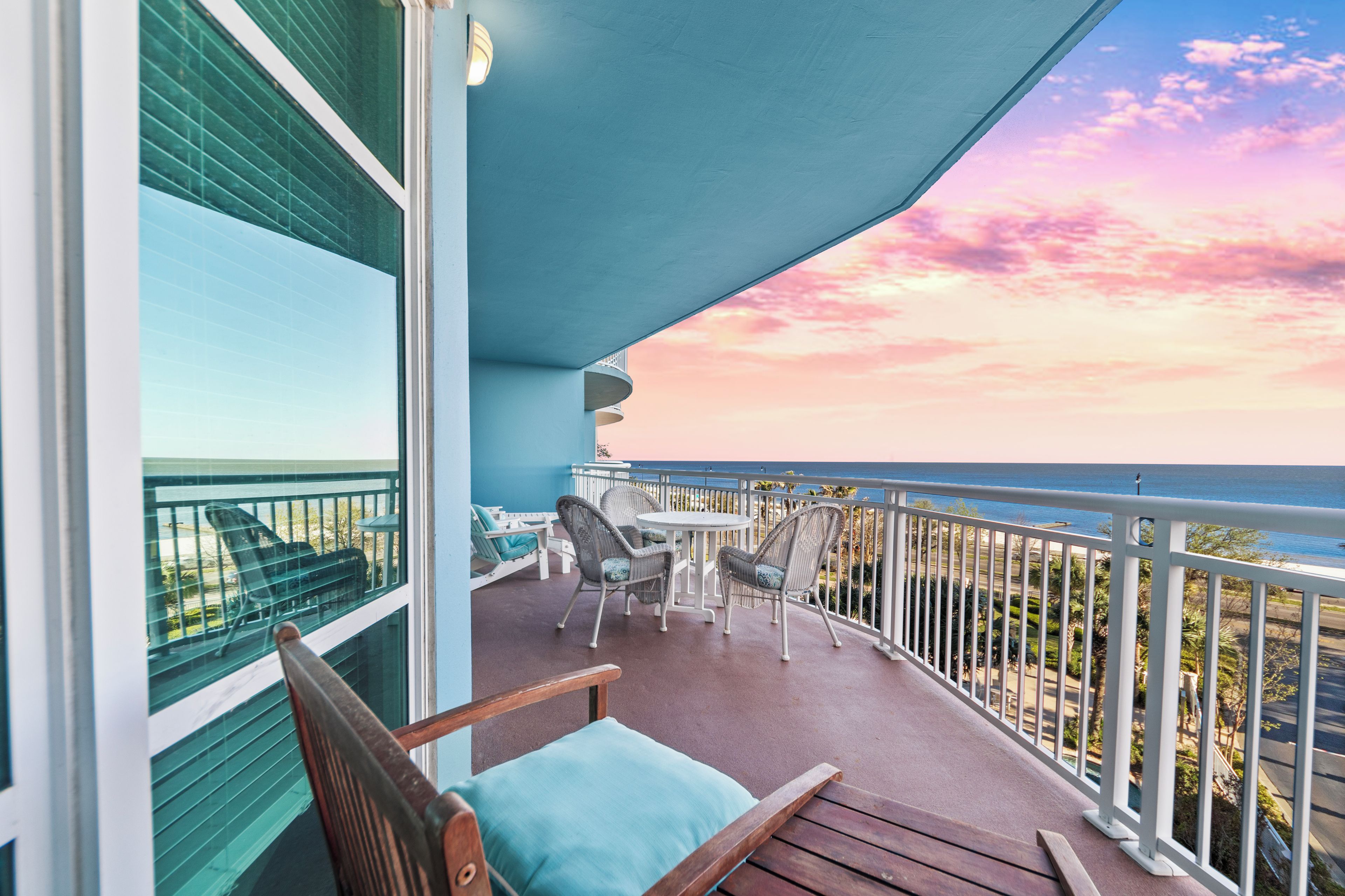A balcony with a view of the ocean, a table with chairs, and a wooden chair.