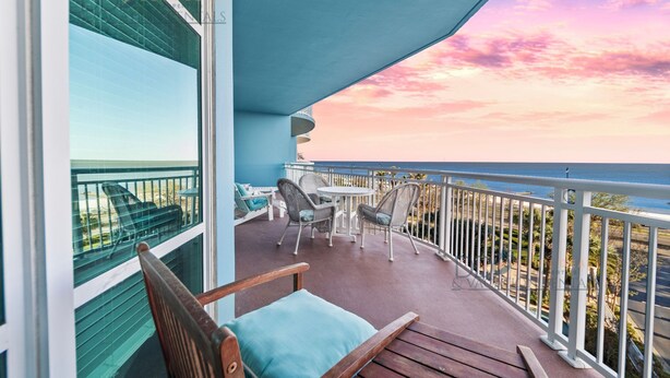 A balcony with a view of the ocean, furnished with wicker chairs and a table, and a wooden bench.