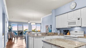 A modern kitchen with white cabinets, a built-in microwave, and a stove. There is a dining area with a table and chairs visible in the background.