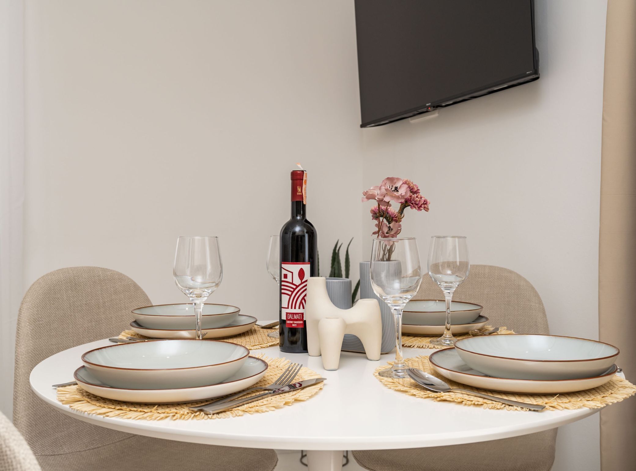 A dining table set with plates, glasses, a wine bottle, and a vase with flowers.