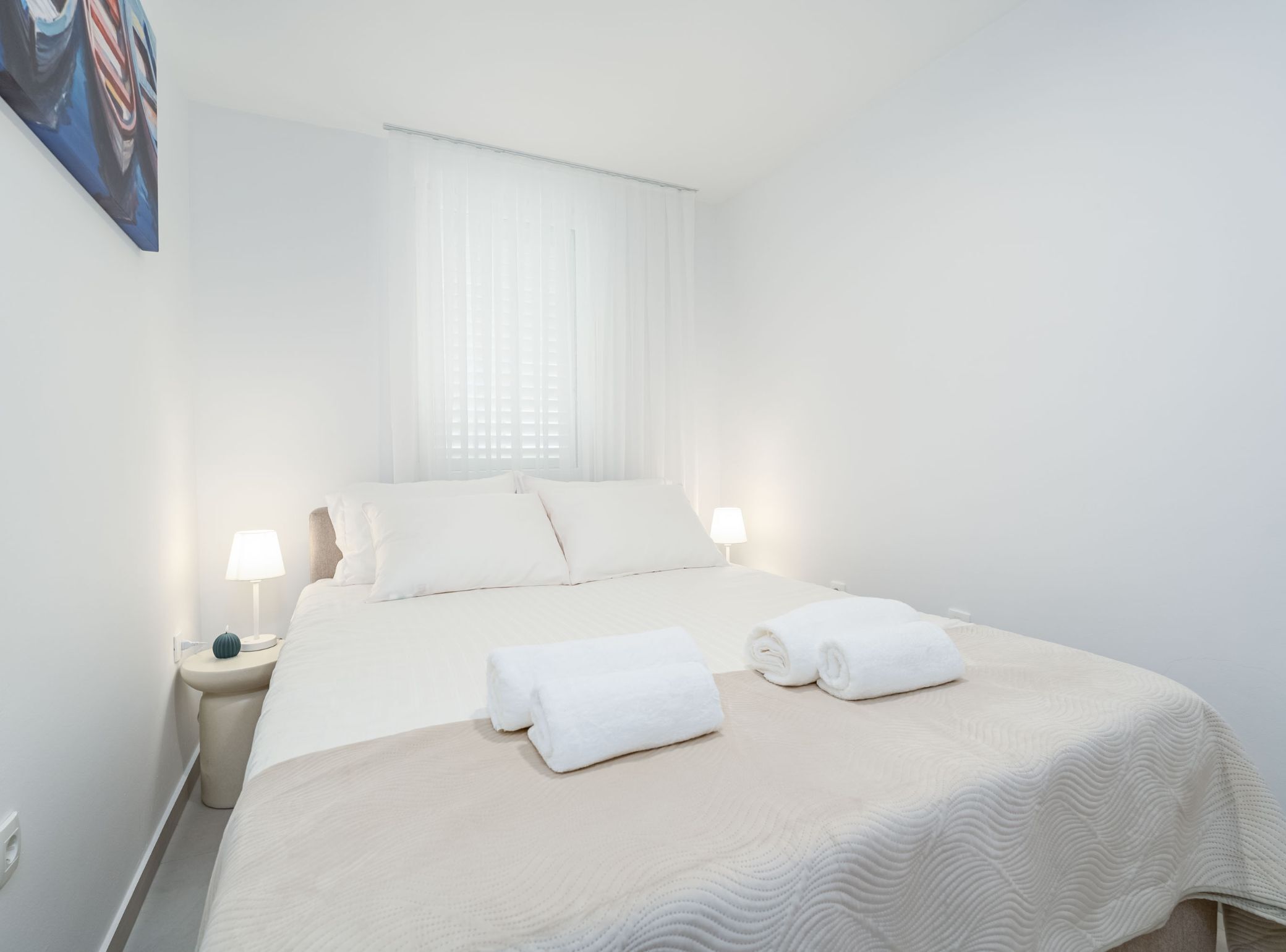 A hotel room with a large bed, two bedside tables with lamps, and a window with blinds.