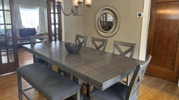 Un comedor con una mesa de madera, seis sillas, una araña y un espejo decorativo.