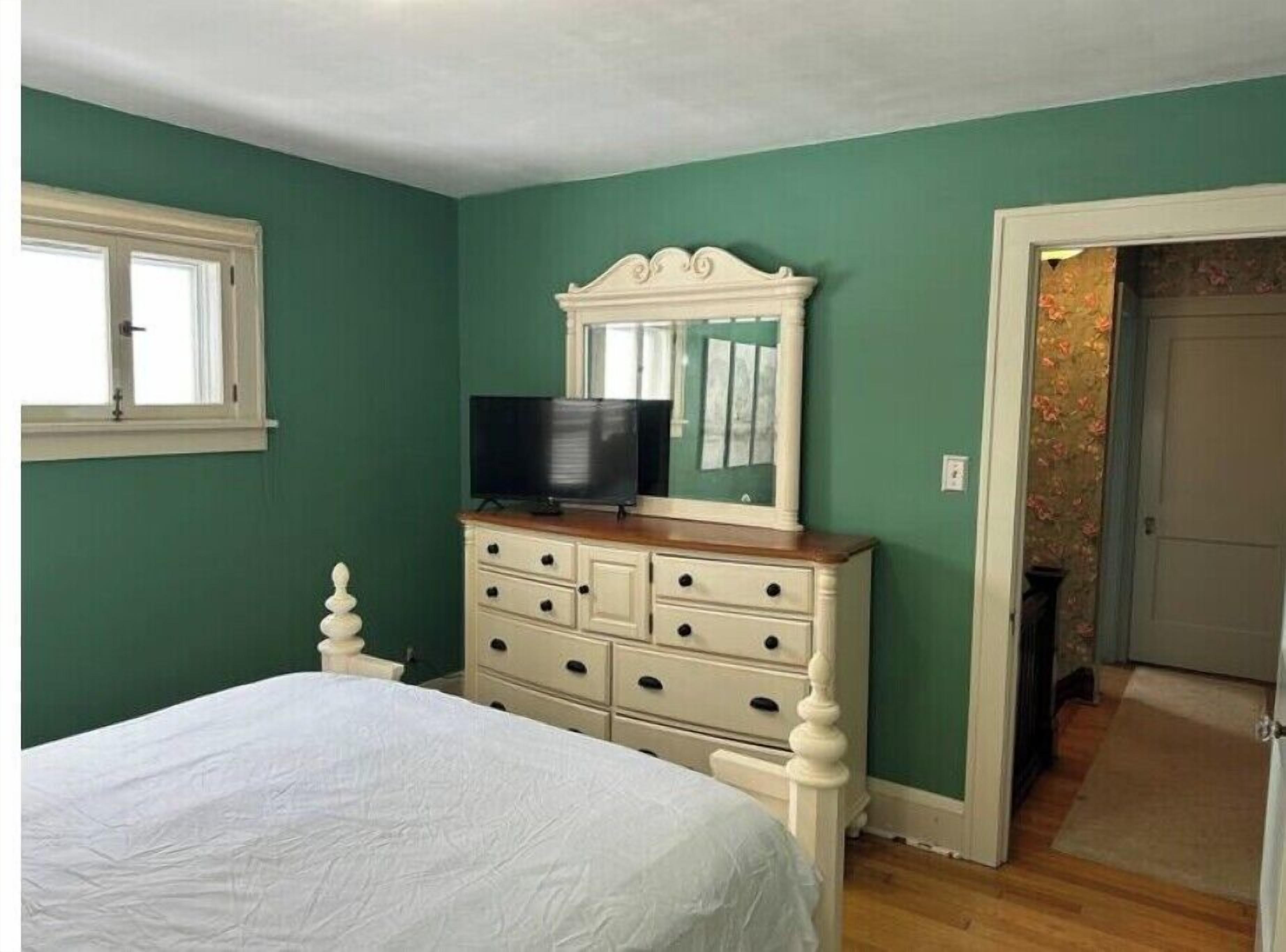 Un dormitorio con cama, cómoda, televisor y espejo.