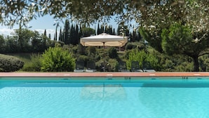 A swimming pool with a sun umbrella, surrounded by greenery and trees. - Green Hill Apt In Tuscan Countryside (Siena)