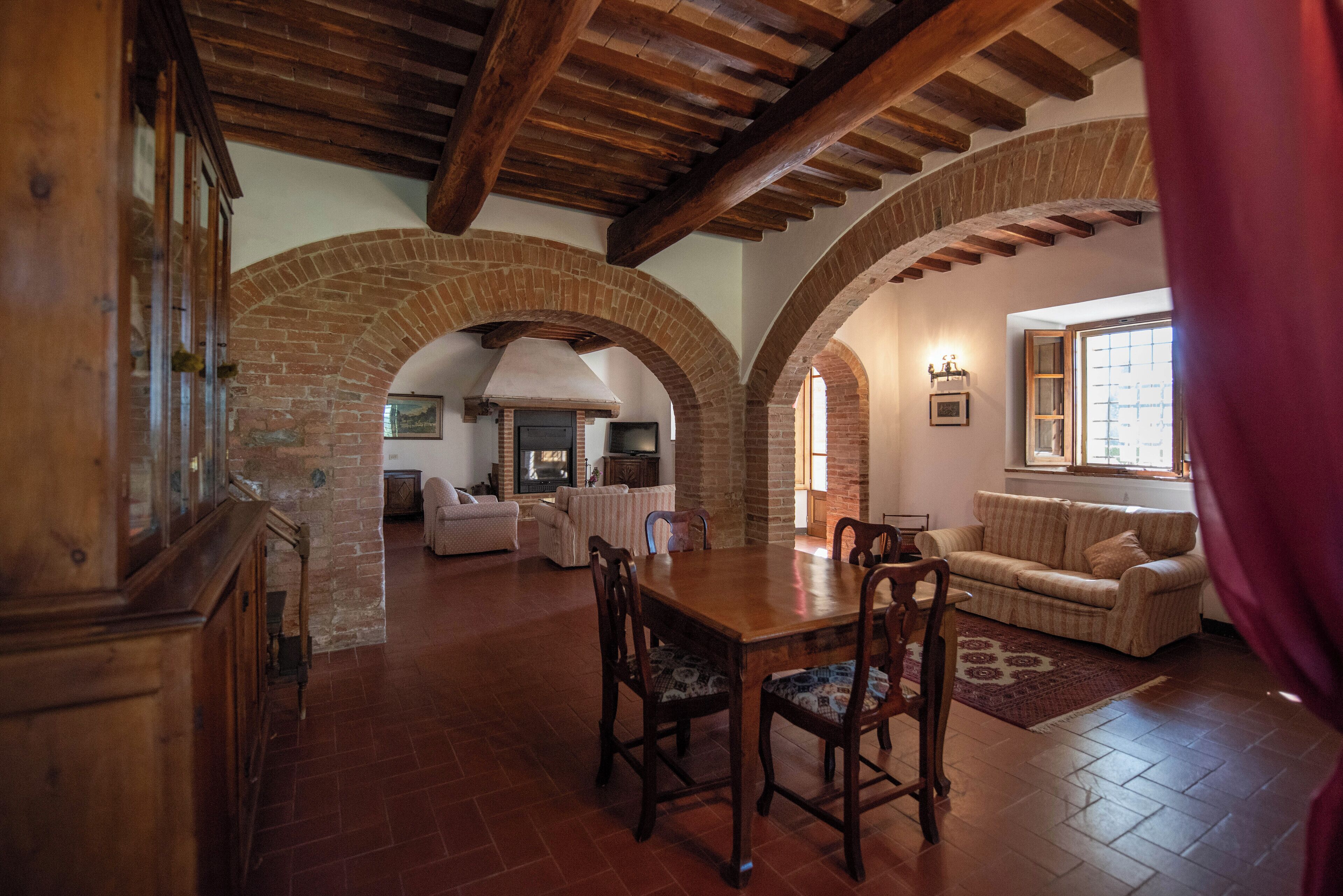 A spacious living area with a wooden dining table, arched brick walls, and a cozy fireplace.