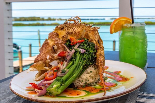 A plate of food with a fish, broccoli, and rice, and a green drink with an orange slice on the side.
