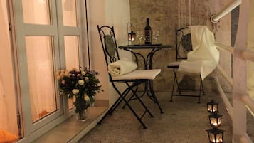 Um quarto pequeno e com pouca luz, com uma mesa e duas cadeiras, um vaso de flores e uma garrafa de vinho.