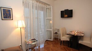 A living room with a sofa, a dining table set for two, a TV mounted on the wall, and a window with sheer curtains. - Old Town Zadar Cozy and Comfy Apartments (Zadar)