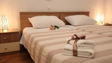Quarto de hotel com duas camas, cada uma com roupa de cama listrada e cabeceira de madeira. Há duas mesas de cabeceira com luminárias, e um pequeno objeto decorativo em uma cama.