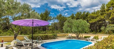 A swimming pool with lounge chairs and a purple umbrella.
