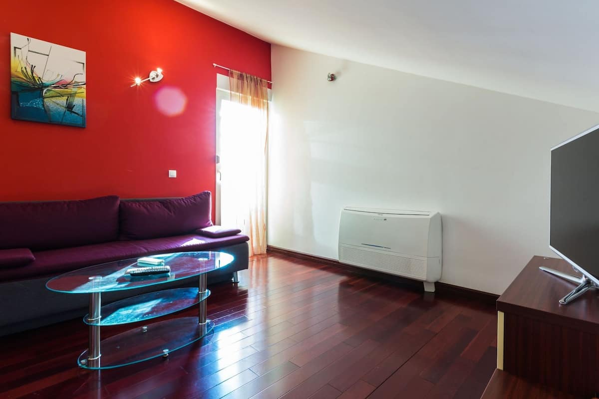 A modern living room with a red accent wall, a purple sofa, a glass coffee table, and a white radiator.