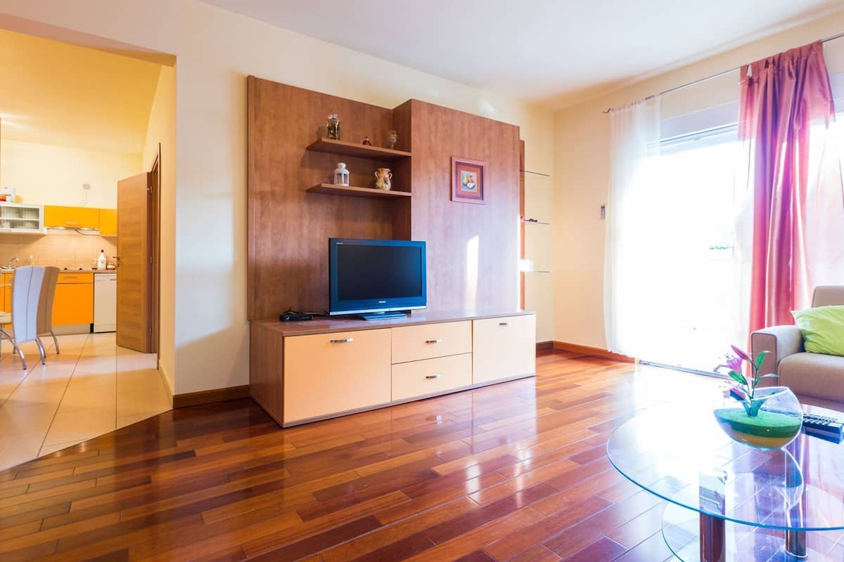 A modern living room with a wooden entertainment unit, a flat-screen TV, and a glass coffee table with a decorative plant.