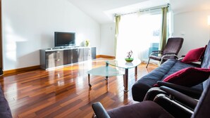A modern living room with a sofa, a glass coffee table, a TV on a cabinet, and a view of the outdoors through large windows. - Elegant and Lavish Leisure Apartments Zadar With Outdoor Pool (Zadar)