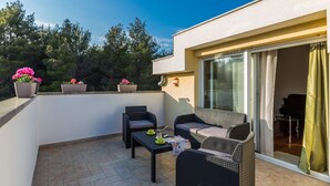 A balcony with wicker furniture, potted plants, and a sliding glass door leading to an indoor area. - Elegant and Lavish Leisure Apartments Zadar With Outdoor Pool (Zadar)
