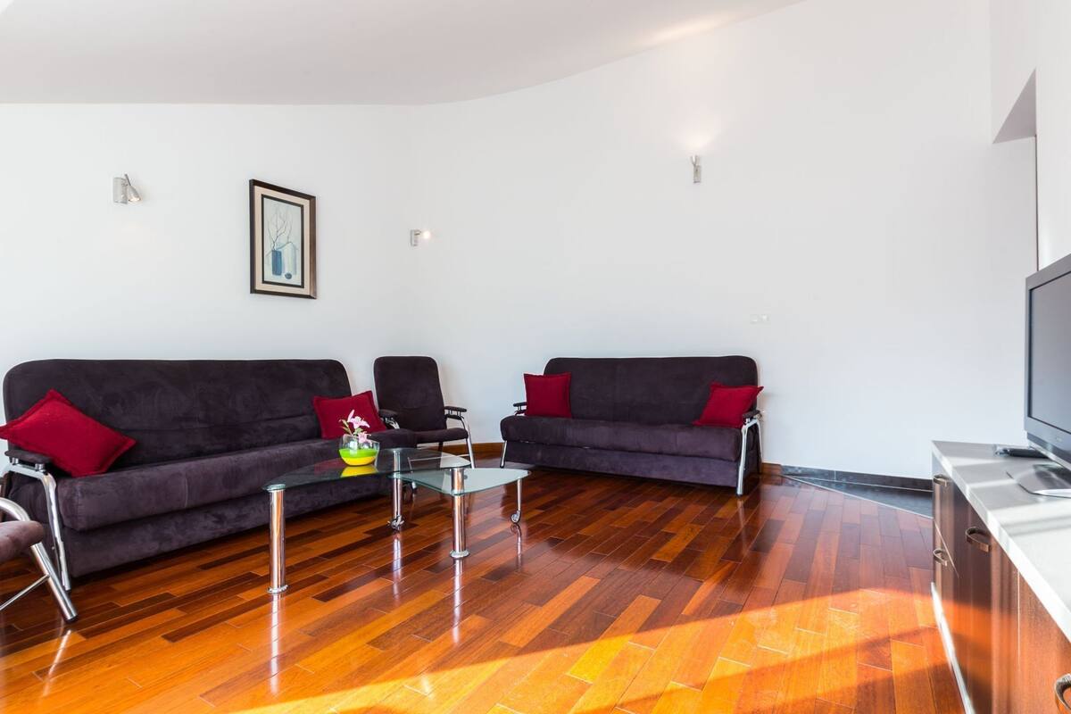 A modern living room with two dark sofas, a glass coffee table, and a flat-screen TV.