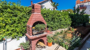Un horno de ladrillo al aire libre con chimenea, rodeado de plantas en macetas y una valla metálica.