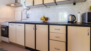 Una cocina con armarios color crema, encimera negra, estufa, microondas y frutero.