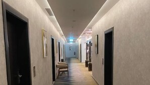 Ein langer, schmaler Korridor mit Türen an beiden Seiten, einem gemusterten Teppich und einer Leuchte an der Decke.