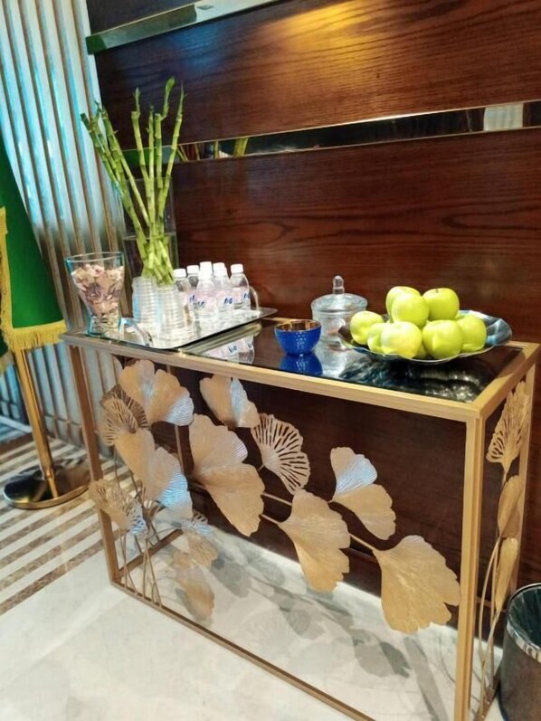 A reception area with a wooden console table displaying water bottles, a vase with green plants, and a bowl of apples.