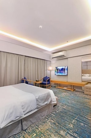 A hotel room with a bed, a desk, a chair, a television, and an air conditioning unit. -  Skoop jeddah (Jeddah)