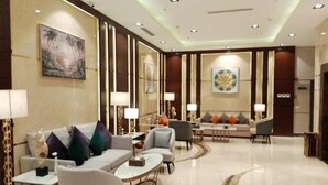 Eine geräumige Lobby mit einer Sofagarnitur, Sesseln und einem Couchtisch. An den Wänden sind Lampen angebracht und über der Couch befindet sich ein großes Dekorationsobjekt.