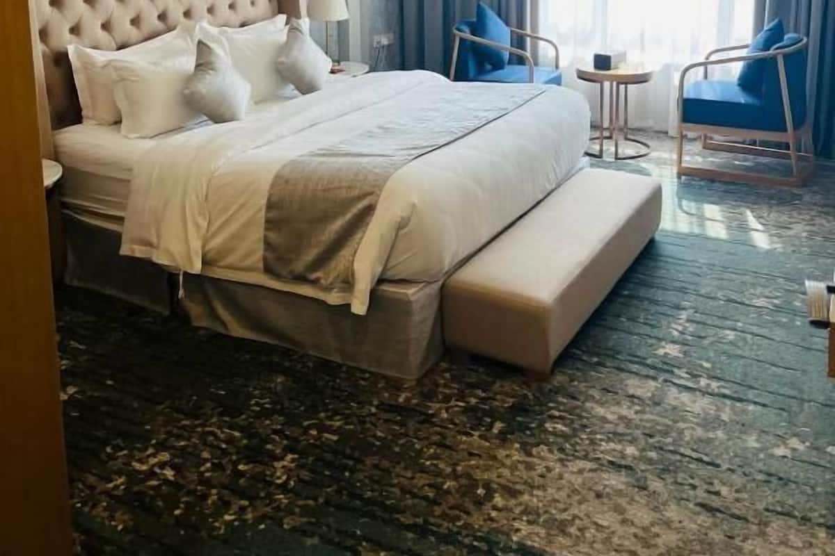 A hotel room with a large bed, a bedside table, a chair, a small table, and a window with curtains.