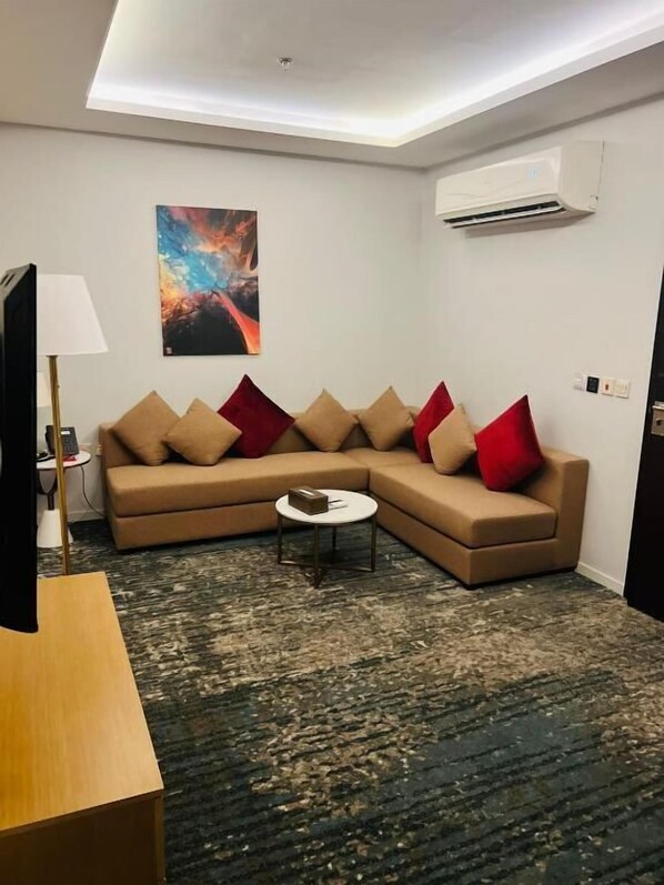 A modern living room with a beige sectional sofa, a small round coffee table, and a flat-screen TV. - Skoop Hotel Jeddah (Jeddah)